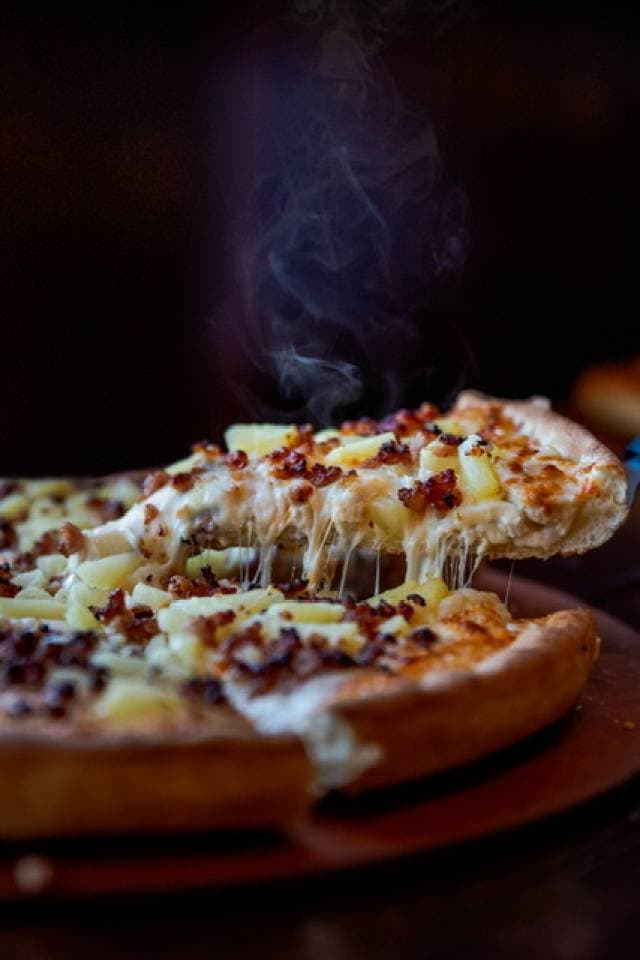 A cheesy pineapple and bacon pizza being served fresh, still steaming